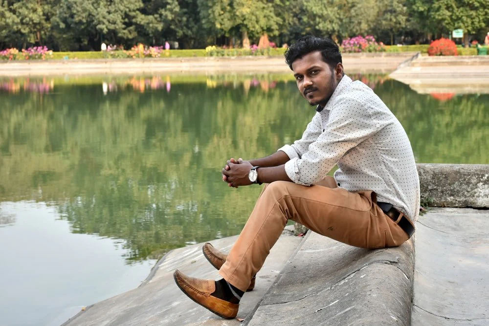 Paint By Numbers | Kolkāta - Boy In White Sweater And Brown Pants Sitting On Gray Concrete Surface Near Body Of Water