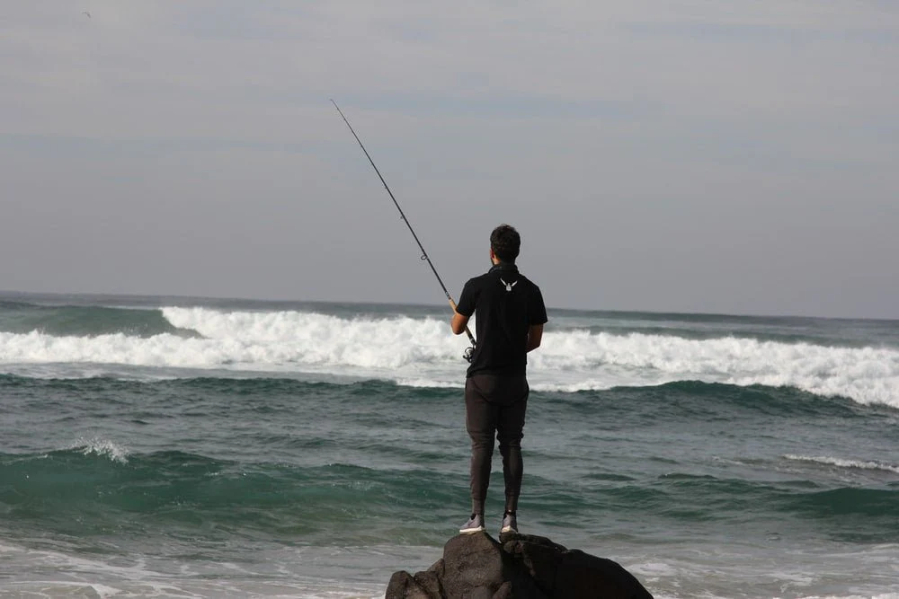 Paint By Numbers | Man In Black Jacket And Black Shorts Holding Fishing Rod Standing On Brown Rock Near Sea